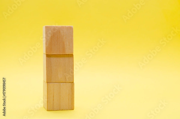 Obraz Stake of wooden cubes on yellow background with customizable space for text or ideas.