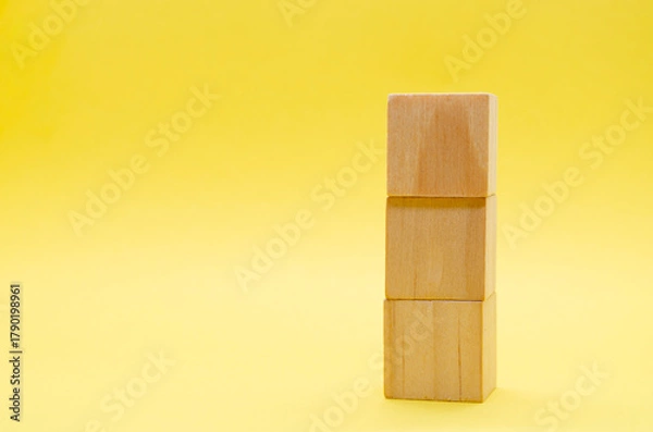 Obraz Stake of wooden cubes on yellow background with customizable space for text or ideas. Copy space concept.