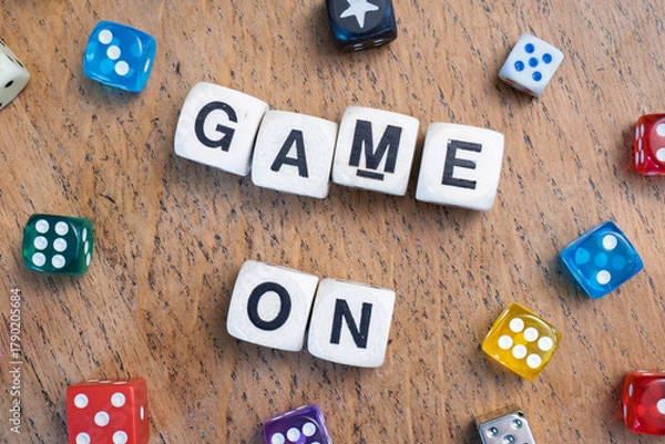 Obraz GAME ON spelt using wooden word dice with vibrant dice set over a pale wooden tabletop background - perfect for promoting game events or fun family gatherings.