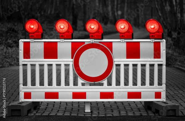 Fototapeta Traffic barring with red battery flash lights indicating road closure, “no entry“ or “do not pass“ at a blocked road. Colorful elements isolated on black and white dark grayscale background.