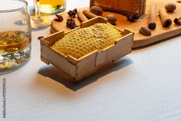 Fototapeta Composition with whiskey, natural honeycomb, and various winter spices on a wooden board. Perfect for holiday drink menus or Christmas concepts. Wide shot with copy space on a white table