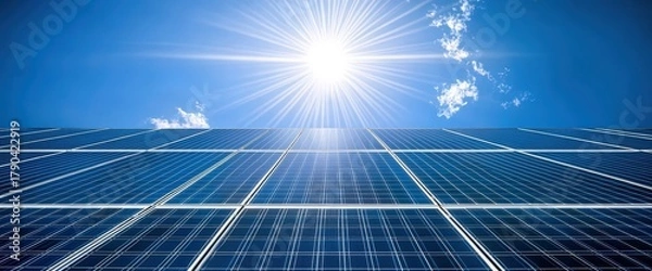 Fototapeta A bright sun shines over a solar panel array, showcasing renewable energy technology against a clear blue sky.