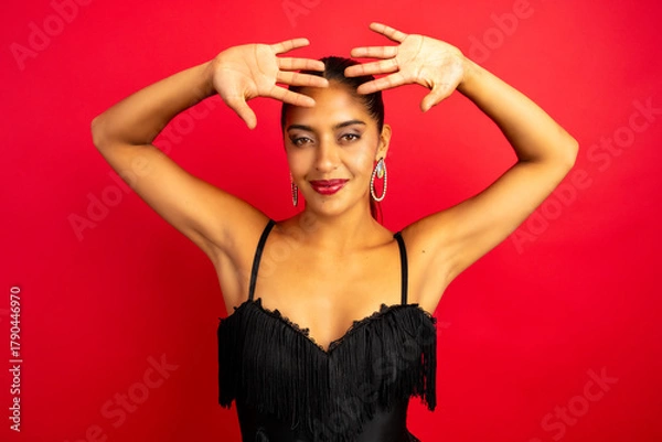 Fototapeta Confident latin woman smiling and raising hands over her head on a red background