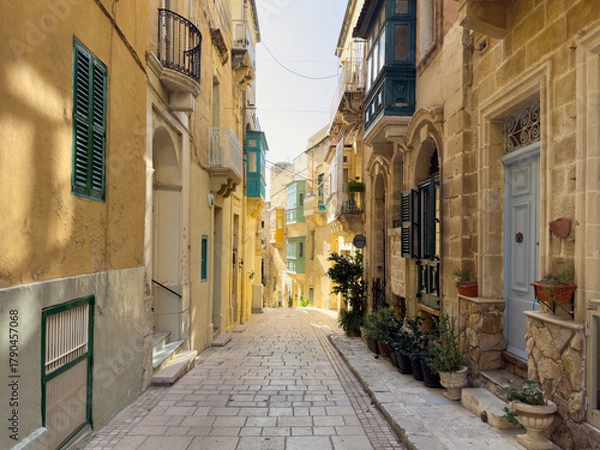 Fototapeta Picturesque view down a classic, gently sloping street in Valletta, Malta. The soft daylight beautifully highlights the detailed limestone facades and the iconic, colorful traditional Maltese wooden b