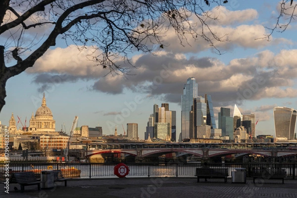 Obraz London, UK Panoramic view of the london skyline from the river thames, contrasting the dome of St. Paul's cathedral with the modern skyscrapers of the city, framed by a bare tree branch.