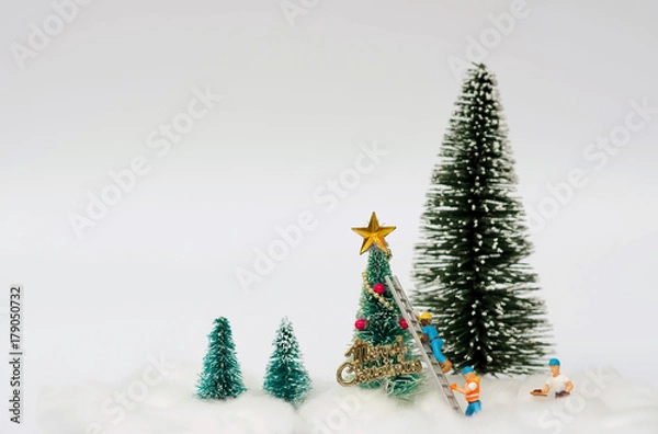 Fototapeta Miniature figure of workers are decorating an artificial Christmas trees with snow background using for Christmas decoration concept.