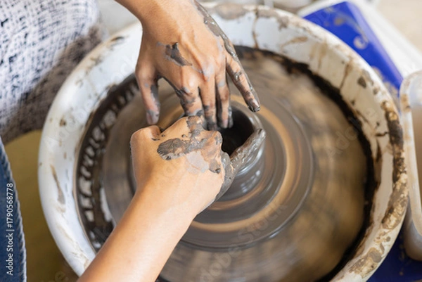 Fototapeta Close up of woman’s hands shaping clay on pottery wheel in selective focus. Handmade ceramic art, artisan craft, traditional pottery process, creative hobby and detailed craftsmanship.