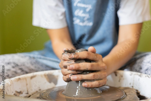Fototapeta Close up of female hands shaping clay on pottery wheel in selective focus. Artistic handmade ceramic, learning pottery craft, creative process, traditional artisan skill, hobby and craftsmanship.