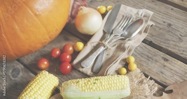 Fototapeta Showing partly husked corn resting on wooden plank, with pumpkin, tomatoes, onion and tied cutlery