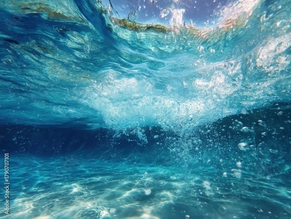 Obraz Underwater view of ocean wave breaking with bubbles and sunlight creating patterns on sand bottom tropical location