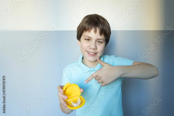 Fototapeta Young boy proudly showing off a yellow toy while smiling against a light background