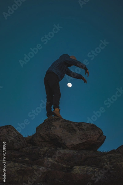 Obraz Silhouette of a man standing on rocks beneath the moon in Norway. A serene Nordic evening filled with silence, space, and the beauty of pure minimalism