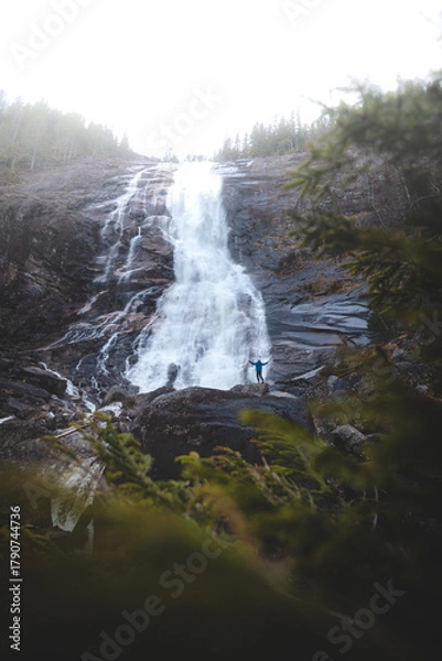 Fototapeta Person standing below powerful Reiarsfossen waterfall in Setesdal Valley, Norway. Dramatic scene showing human scale against raw Nordic nature and water energy