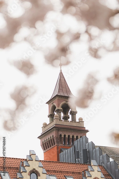 Fototapeta Architectural detail of historic tower in Kristiansand, Norway, framed by blooming cherry trees. Blend of culture, history, and nature in Nordic springtime
