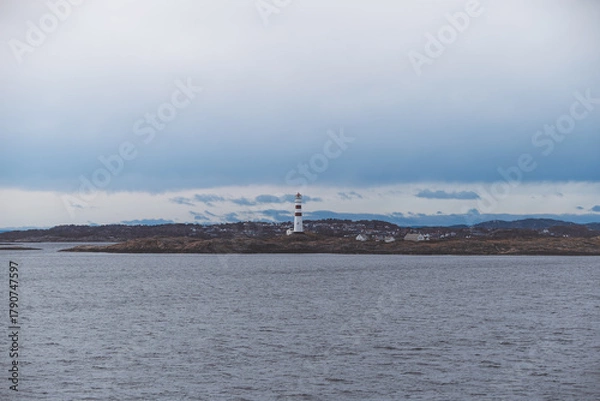 Fototapeta Lonely lighthouse standing on the rocky coast near Kristiansand, Norway. Calm Scandinavian seascape under a moody sky capturing the spirit of coastal solitude.