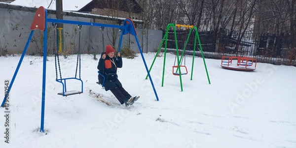 Fototapeta A happy 48-year-old woman swings on a swing at a snowy playground in winter.