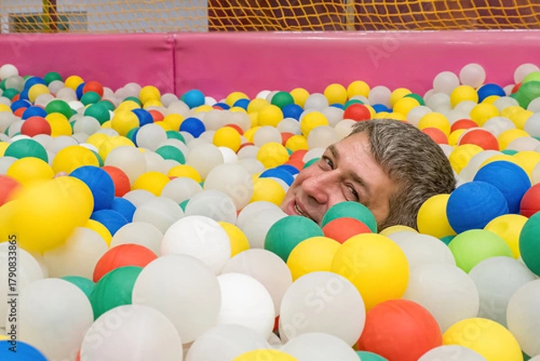 Fototapeta A smiling man against a background of colorful plastic balls. A festive event.