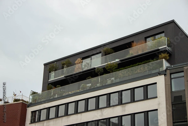 Fototapeta Modern building with sleek architecture featuring multiple balconies adorned with greenery, showcasing urban living and contemporary design aesthetics in a metropolitan environment