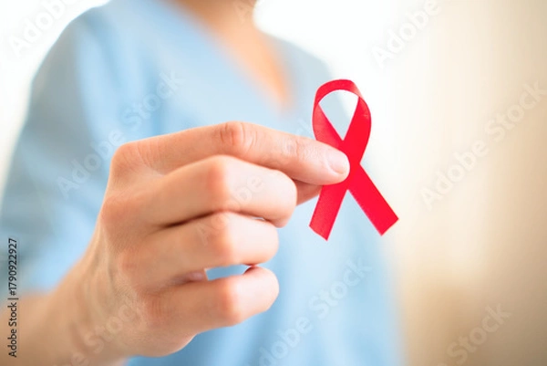 Obraz Extreme close up of female hand holding red satin awareness ribbon, symbolizing HIV AIDS solidarity, support and hope for future treatment.