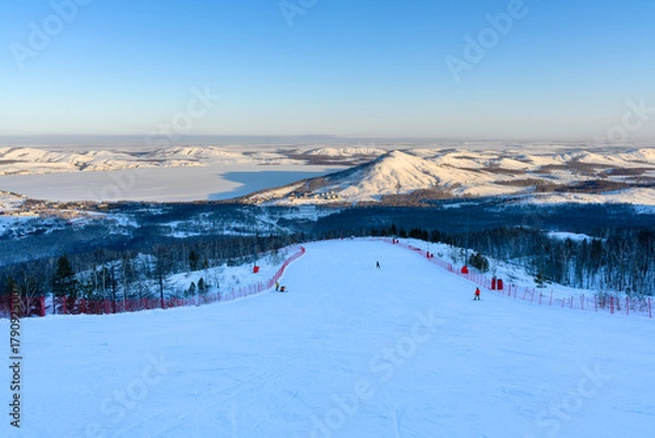 Obraz Steep ski slope at sunset against the backdrop of the picturesque landscape of the Ural Mountains.