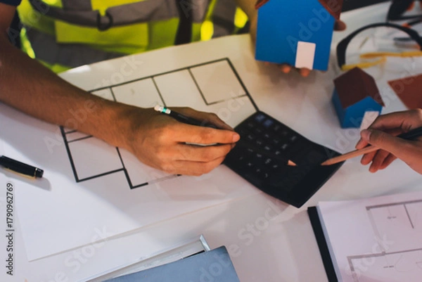 Fototapeta Closeup of team of industrial engineers meeting analyze machinery blueprints consult project on table in manufacturing factory. Working in manufacturing plant or production plant.