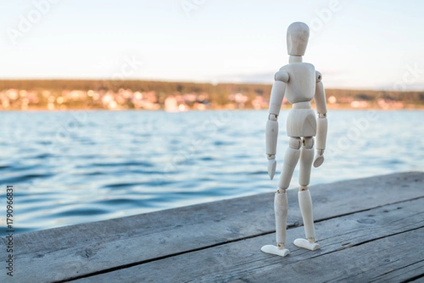 Fototapeta The wooden figure resembles a man standing against the background of a lake