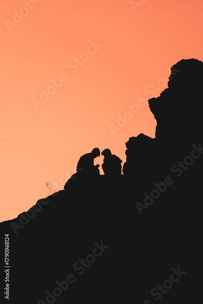 Fototapeta A couple is silhouetted against a backdrop of a sunset