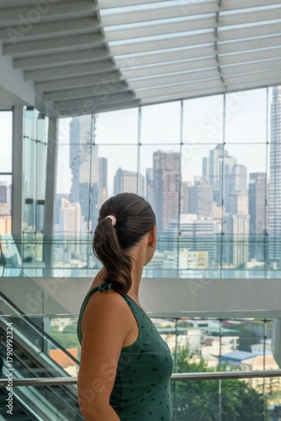 Fototapeta Woman looking at modern city skyline from glass building, symbolizing aspiration, travel, and modern lifestyle concept