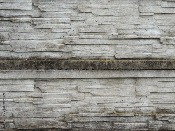 Fototapeta a fragment of an old, dilapidated, mossy concrete-stone fence with a rough, destroyed texture of the masonry, green traces of wet moss and an uneven structure of the stone layers