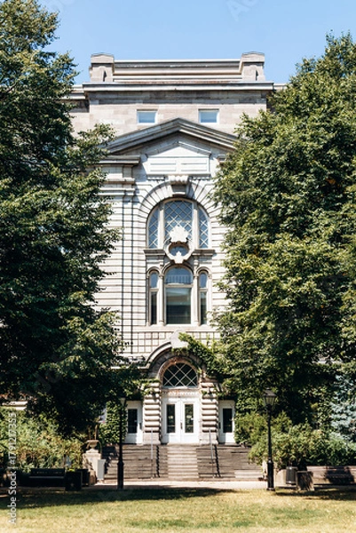Fototapeta Montreal, Canada - August 11, 2025: Historic building facade surrounded by green trees in Old Montreal