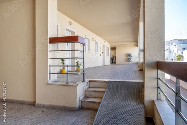 Fototapeta Bright and spacious entrance to a modern building featuring a wheelchair-accessible ramp and well-maintained walkway with potted plants
