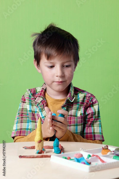 Fototapeta Caucasian boy is crafting with colorful modelling clay.