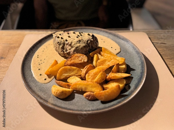Obraz close up of steak with creamy peppercorn sauce and roasted potatoes on a plate at a restaurant outdoors at night 