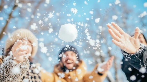 Fototapeta Happy friends enjoying a playful snowball fight in a snowy winter park, with a snowball in mid-air and falling snowflakes.