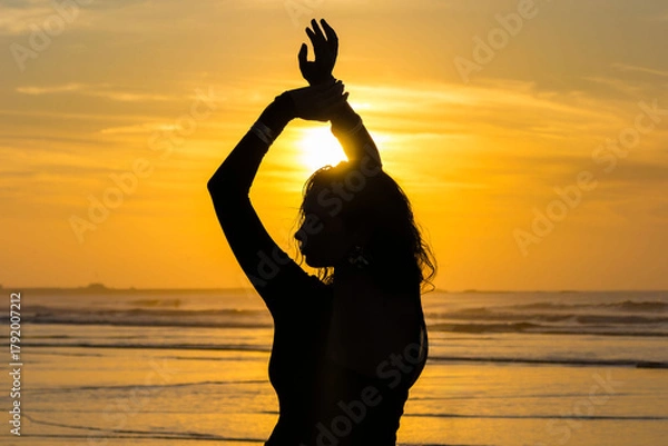 Obraz Silhouette of woman dancing on the beach at sunset with sun above the sea.