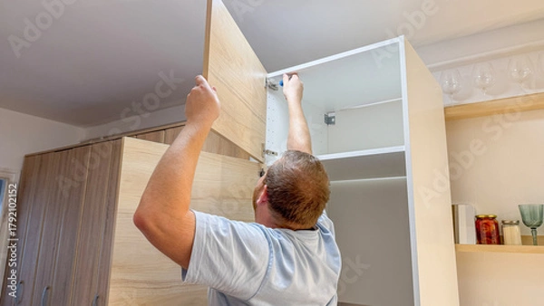 Fototapeta A Caucasian man meticulously assembles a cabinet, celebrating DIY Day and International Handyman Appreciation Week