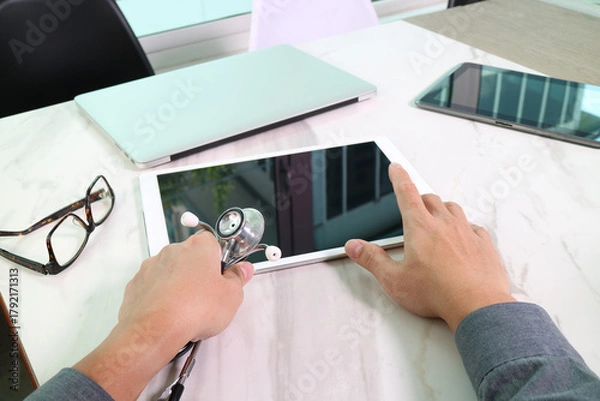 Obraz Doctor using tablet computer with stethoscope on desk