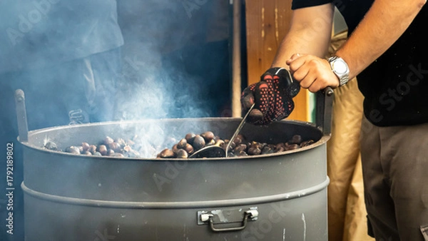 Obraz roasting chestnuts in large metal drum with smoke rising