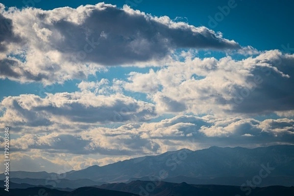 Fototapeta Dramatic sky filled with thick, textured clouds over a distant mountain range on a clear day