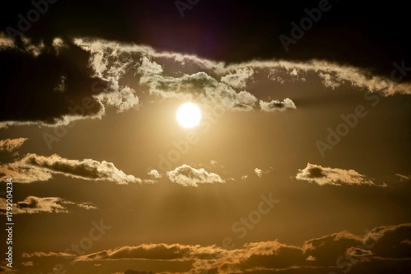 Fototapeta Dramatic golden sunset with sun shining through dark clouds creating a moody and atmospheric sky scene