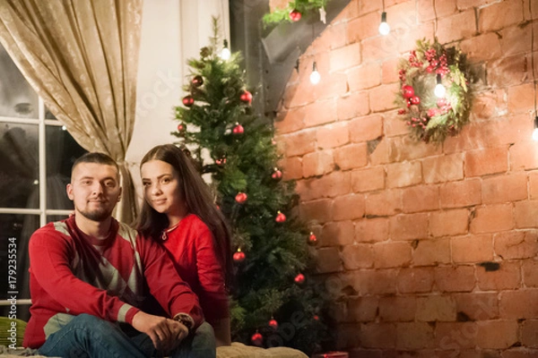 Fototapeta Beautiful happy young family celebrating Christmas together. Lovers on the New Year together in an apartment in the Loft style. Bedroom apartment Loft decorated in New Year's style.