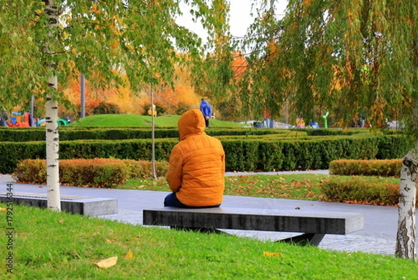 Fototapeta A man resting on a bench in an autumn park, autumn landscape in the city