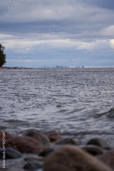 Obraz Distant city skyline over Gulf of Finland with stones and waves in foreground.