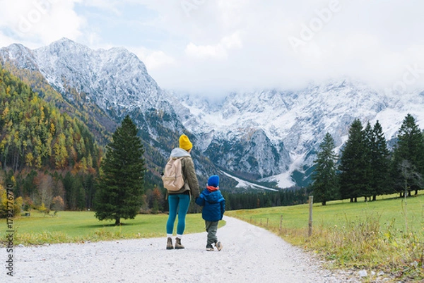 Fototapeta Family hiking together in nature. Woman with son running on road with mountain view in autumn. Mother and child together outdoors. Adventure travel with kids in nature.