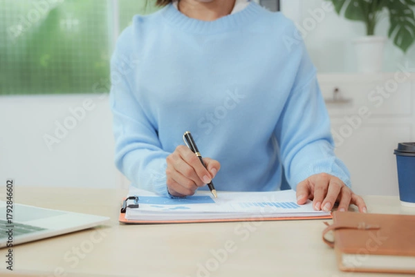 Fototapeta Businesswoman smiling while using laptop and talking on mobile phone at desk in office and at home or coffee shop.