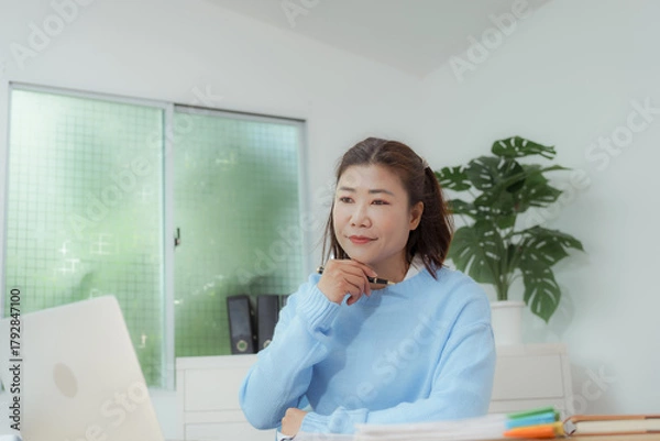 Fototapeta Businesswoman smiling while using laptop and talking on mobile phone at desk in office and at home or coffee shop.