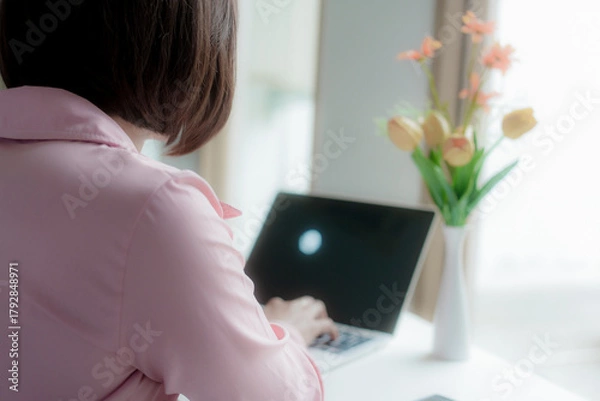Fototapeta Businesswoman smiling while using laptop and talking on mobile phone at desk in office and at home or coffee shop.
