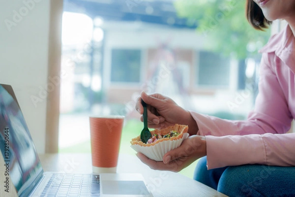 Fototapeta Businesswoman smiling while using laptop and talking on mobile phone at desk in office and at home or coffee shop.