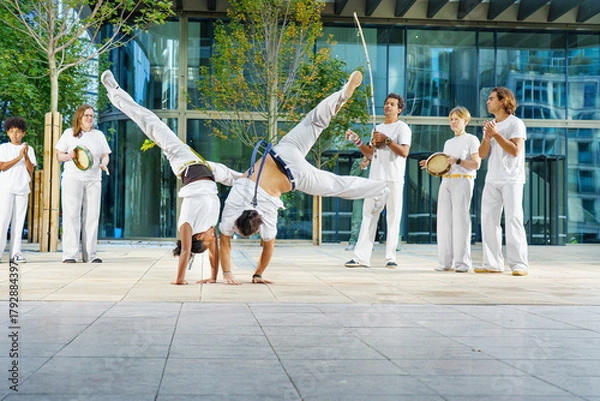 Fototapeta A group of sporty people of different ages training capoeira in a big city