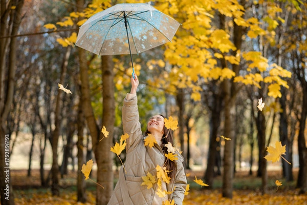 Obraz Conceptual portrait of woman in autumn park lifting umbrella with falling yellow maple leaves